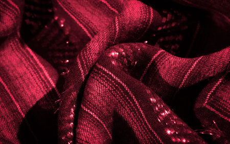 the crimson fabric ripples with a textured shine, showing intricate woven patterns that reflect the light, adding depth and dimension to the textile's rich color and surface.の写真素材