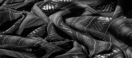 Blurred view of a dark, textured fabric with a geometric pattern, showing subtle light reflections across the woven surface. The fabric features intricate design details in a modernの写真素材