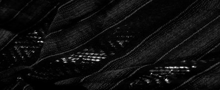 Blurred close-up shot of a textured black fabric with intricate striped and geometric patterns. The...