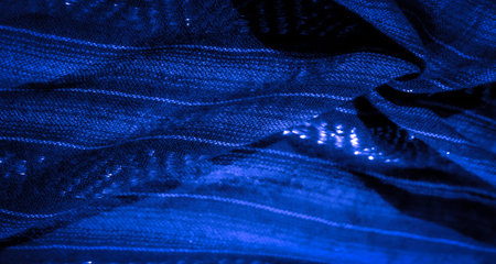 Blur the intricate folds and shiny textures of dark blue fabric with glowing highlights scattered across the surface, creating a mesmerizing abstract visual experience.の写真素材