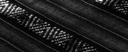 Blurred black and white fabric with diagonal woven patterns and reflective surfaces. The fabric's...