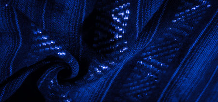 Blurred abstract shot of a folded blue fabric with intricate sparkling details. The subtle...