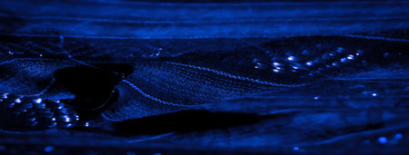Blur the interplay of light and dark contrasts across this blue fabric's textured surface, highlighting the intricate weaving pattern and subtle glow, evoking a sense of modern elegance.の写真素材
