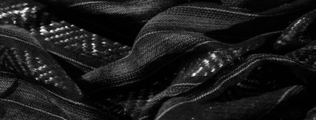 Blurred close-up of a draped fabric with glossy, woven geometric details. The play of light on the...