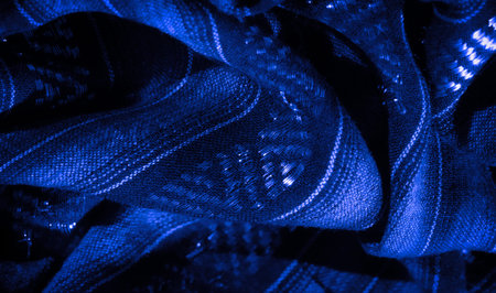 Blurred close-up of textured blue fabric with shimmering light highlights, presenting a smooth flow...