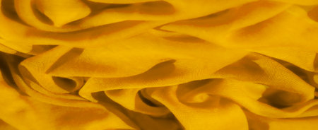 Blurred close-up of a yellow fabric with soft, textured folds creating an elegant swirl pattern. The delicate transparency and smooth surface of the material are gently illuminatedの写真素材