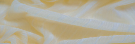 Blurred soft yellow fabric with subtle stripes flowing gently in overlapping folds. The textured surface captures the light, creating a soft, radiant glow across the delicate material.の写真素材