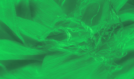 Blur of bright green fabric with delicate threads gently swirling across the surface, creating a soft and flowing texture. The intricate details capture the fine weaving and glowing highlightsの写真素材