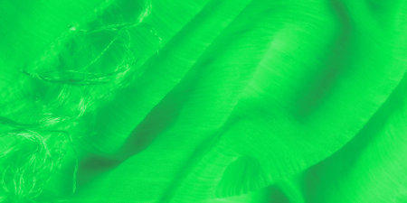 Blur of soft green fabric featuring glowing, flowing threads. The material's intricate weaving and delicate texture catch light, creating a luminous surface with smooth folds and organic movement.の写真素材