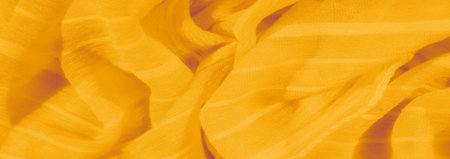 Blur of textured yellow fabric, featuring soft folds and gentle creases. The fabric's delicate threads add depth to the smooth surface, reflecting light with a soft glow.の写真素材