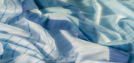 Blur of blue fabric with thin stripes, highlighted by a gentle shimmer and natural folds. The light plays across the surface, accentuating the fabric's soft texture and flowing design.の写真素材