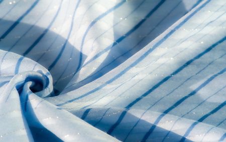Blur of light blue fabric with soft folds and subtle stripes, illuminated by gentle light reflections, creating a delicate and calming visual texture of flow and softness.の写真素材