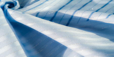 Blurred abstract blue fabric with soft waves and shimmering lines, illuminated by sunlight. The smooth texture and light reflectivity create a serene, flowing effect, perfect for design use.の写真素材
