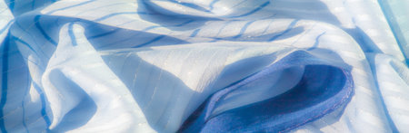 Blur of delicate blue fabric with vertical striped patterns. The light sparkles off the surface, giving it a shimmering and flowing appearance, with soft folds in the material.の写真素材