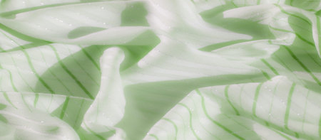 Blur, soft and delicate green fabric adorned with shimmering accents and thin white stripes. The gentle folds in the fabric create a dynamic and glowing appearance.の写真素材