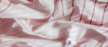 Blur of light pink fabric with shimmering silver accents and red stripe patterns, delicately folded to create elegant waves that reflect light and enhance the luxurious appearance.の写真素材