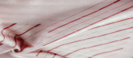 A soft, flowing pink fabric featuring a wavy red pattern accented with subtle silver lines. The gentle folds create a textured and elegant appearance, perfect for fashion or design concepts.の写真素材