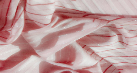 Blurred image of soft pink fabric with red and silver stripes, highlighting the delicate texture and abstract flowing design. The shimmering silver accents add elegance and luxury to the textile.の写真素材