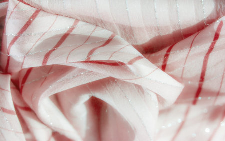 Blur of delicate pink fabric with elegant red curved lines and silver details, creating a flowing...