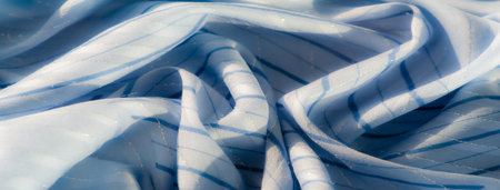 Blur of shimmering light blue fabric with reflective surfaces and a subtle striped pattern. The soft...