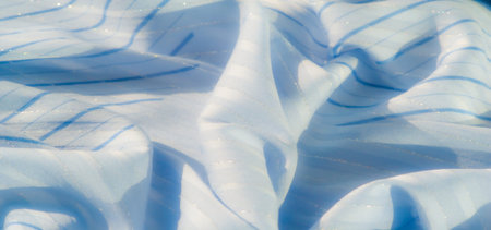 Blur of light blue fabric featuring horizontal stripes and glimmering details. The fabric creates elegant flowing shapes with smooth, soft textures and light reflections.の写真素材
