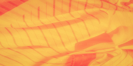 Blur of golden yellow fabric with a rich orange undertone and subtle striped texture. The soft folds and flowing material add depth to this abstract design, evoking a sense of warmth and motion.の写真素材
