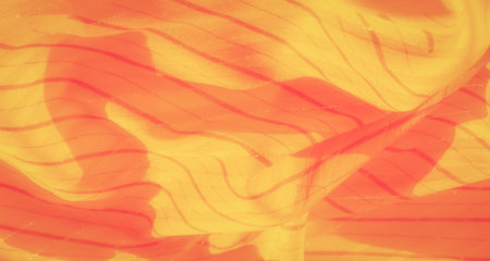 Blurred layers of yellow fabric create a dynamic visual effect with hints of red stripes, resulting in a radiant and captivating design that adds depth and warmth to the overall composition.の写真素材