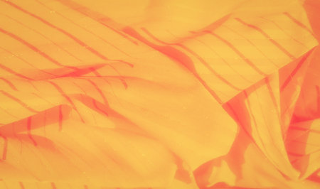 Blur of yellow fabric with glowing orange hues and a striped pattern. The soft, flowing folds of the...