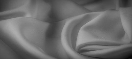 Blurred grayscale fabric gently drapes into soft folds, capturing the play of light and shadow across the surface. The smooth, minimalist texture exudes calm and sophistication.の写真素材
