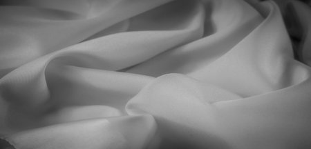 Blurred grayscale fabric with soft folds and smooth textures that create a gentle play of light and...