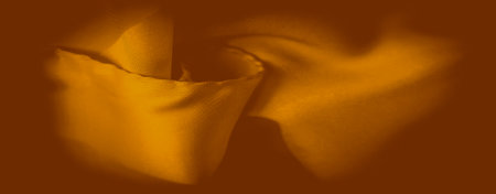 Blurred golden-orange fabric folds gently in waves, creating a serene and elegant flow of texture. The light reflects softly off the surface, accentuating the fabric's luxurious feel.の写真素材