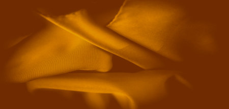 Blurred orange fabric flows in smooth, undulating folds, reflecting warm, golden light. The intricate weave of the fabric adds depth to the image, making it perfect for abstract or textile-focused designs.の写真素材