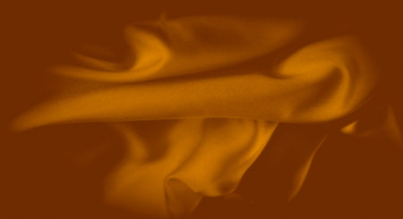 Blurred folds of golden-orange fabric create a soft, flowing texture that exudes warmth and elegance. The intricate weave and gentle lighting give the fabric a luminous quality.の写真素材