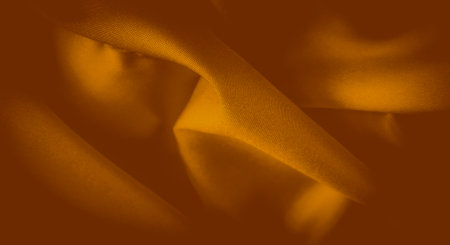 Blurred close-up of a golden fabric with smooth folds and delicate texture, creating a warm and elegant appearance. The soft light enhances the richness of the material, giving it a luxurious sheen.の写真素材