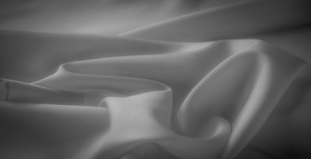 Blurred details of this grayscale fabric reveal soft curves and folds, with a smooth texture illuminated by natural light. The elegant shadows enhance the minimalistic and abstract composition.の写真素材