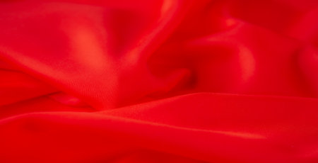 Blur of smooth, bright red fabric, elegantly draped with soft folds. The vibrant red hue and luxurious texture create an eye-catching, dynamic pattern that flows across the fabric.の写真素材