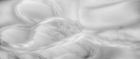 Blurred image of white satin fabric with soft braided strands and smooth folds. The light reflection enhances the glossy texture, creating an elegant and luxurious feel.の写真素材