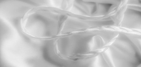 Blurred image of flowing white fabric with soft braided strands that create a fluid, elegant look. The folds and texture of the material are highlighted by the soft light.の写真素材