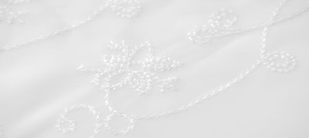 Blur. A white fabric featuring subtle, floral-like embroidery patterns draped softly. The smooth, delicate folds enhance the luxurious feel, perfect for fashion, wedding, or elegant home interiors.の写真素材