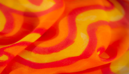 Blur of warm orange and yellow fabric with fluid swirling patterns. The folds of the fabric create a...