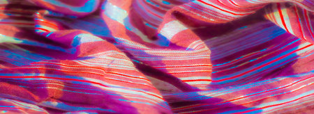 Blurred view of maroon fabric with metallic silver and red stripes, forming delicate folds that...