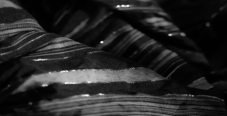 Blur, soft black fabric with fine vertical stripes, intricately woven to create a shimmering effect. The folds create depth and an artistic play of light and shadow.の写真素材