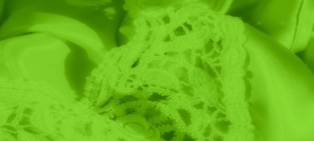Blurred bright green satin fabric layered with intricate lace, showing a detailed floral pattern. The soft folds and reflective surface of the satin create an elegant contrast with the textureの写真素材