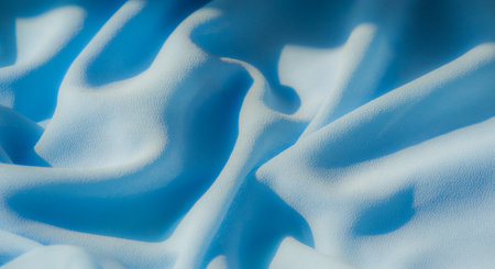 Blur of light blue fabric flowing in smooth, continuous folds. The soft, velvety texture and fluid movement are highlighted by subtle lighting, adding depth and tranquility to the image.の写真素材
