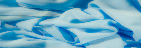 Blur. A vibrant light blue fabric with soft ripples and smooth folds. The textured surface interacts gracefully with the light, creating an elegantの写真素材