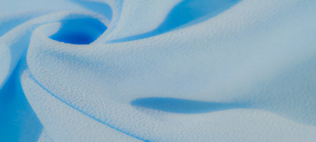Blurred image of bright blue fabric with soft, flowing folds and a subtle texture. The curves create a dynamic, abstract composition with soft light and shadows.の写真素材