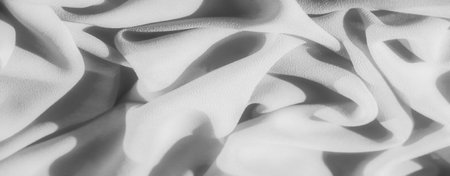 Blurred fluid folds of fabric create a soft, monochrome texture with intricate shadow details. The grayscale composition highlights the elegant drapery and flowing nature of the material.の写真素材