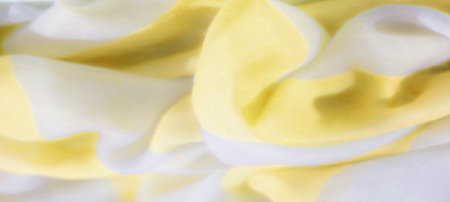 Blur of soft yellow and white fabric intertwined, forming gentle folds with a flowing and smooth texture. The light adds a delicate shimmer to the fabric's translucent quality.の写真素材