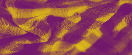 Blur of yellow fabric with intricate folds and a classic checkered pattern. The fabric's rich...