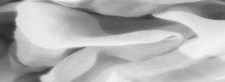 Blurred close-up of grayscale fabric displaying a soft, airy texture with visible folds. The light...